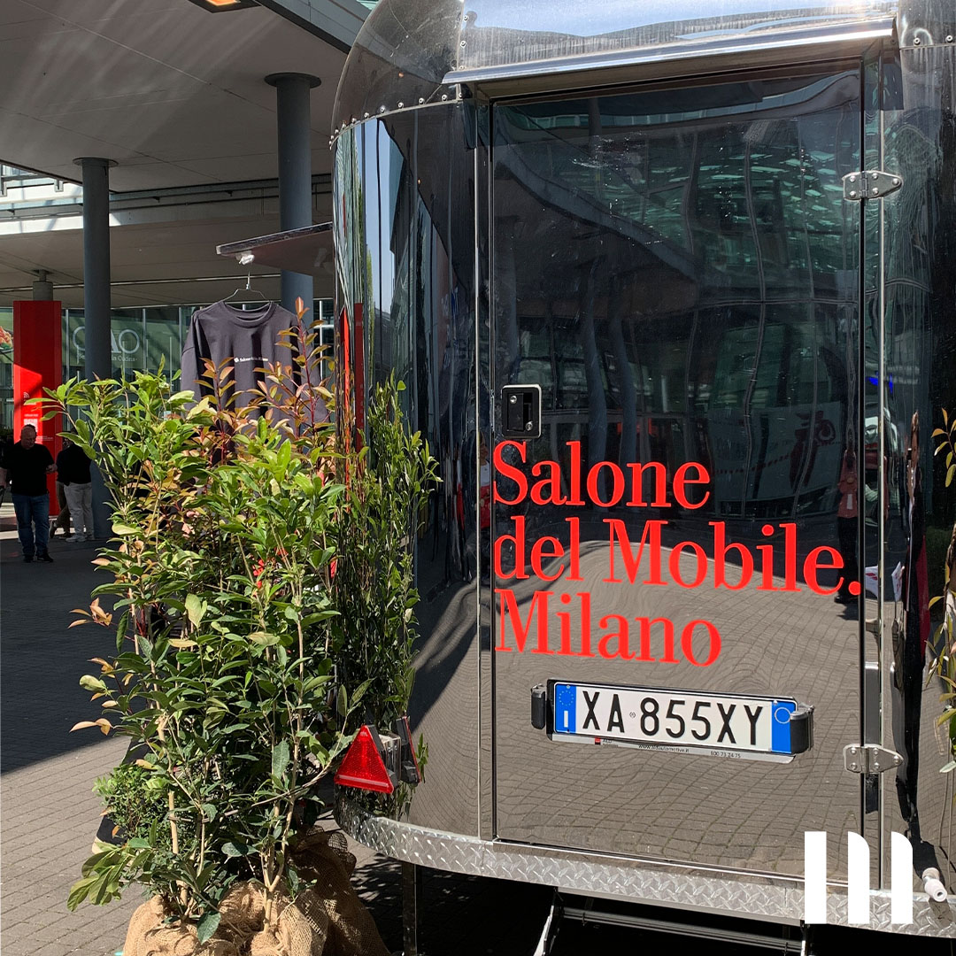 Glänzender Airstream-Trailer mit rotem Schriftzug ‚Salone del Mobile. Milano‘, flankiert von grünen Pflanzen im Eingangsbereich der Möbelmesse.