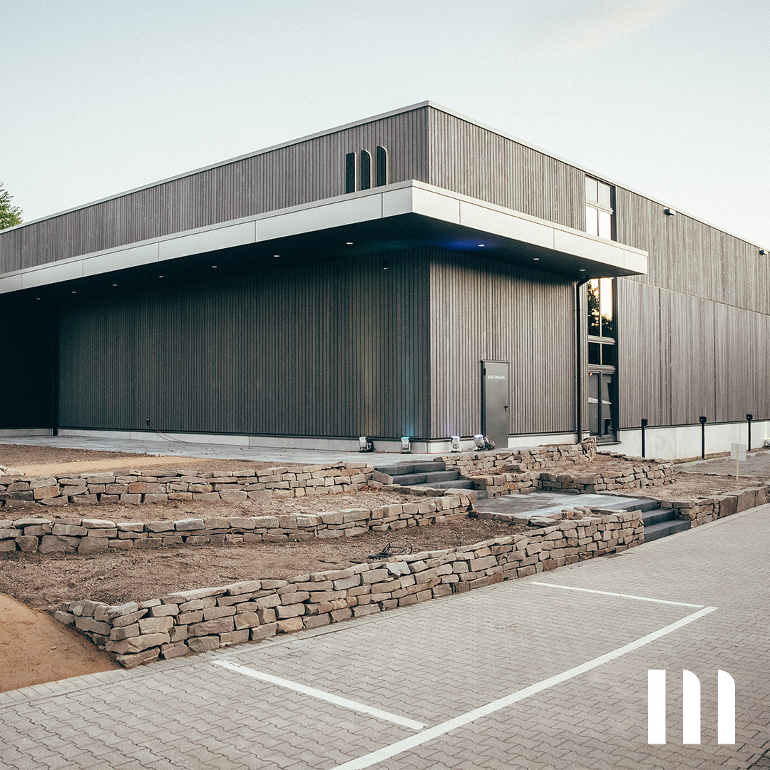Moderne Holzfassade des neuen ppm-Gebäudes mit Natursteinmauer und großzügigem Eingangsbereich
