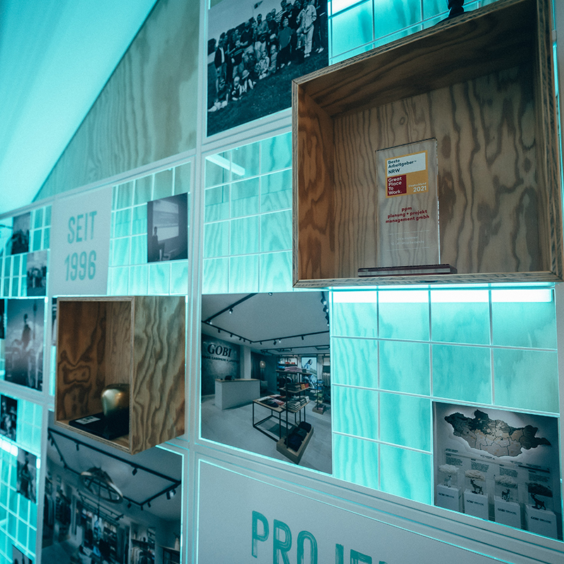 Unternehmenswand mit Auszeichnungen, Projekteinblicken und Firmengeschichte im modernen Büro