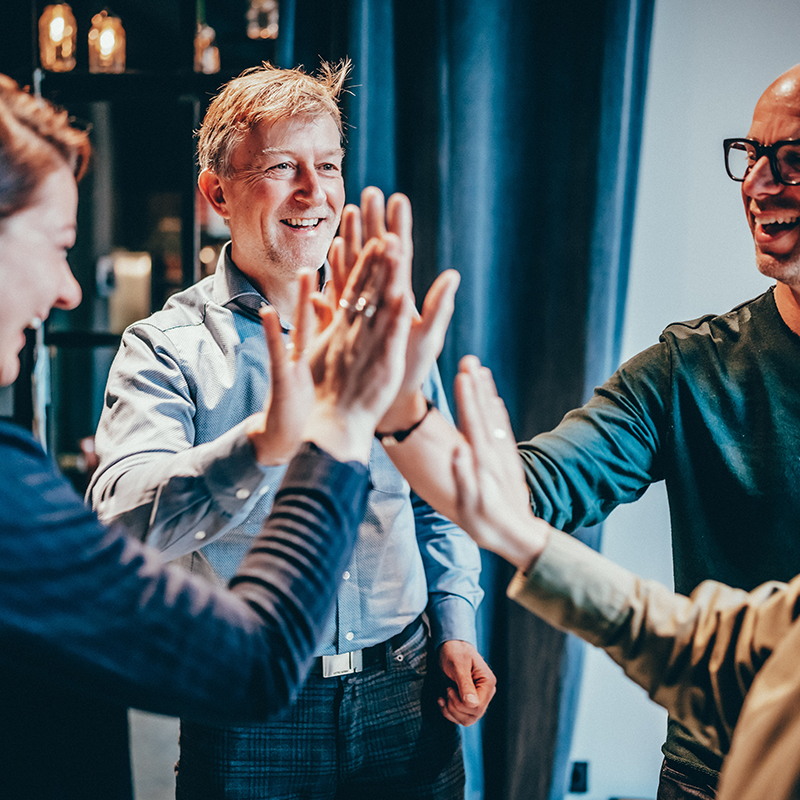 Team feiert gemeinsamen Erfolg mit High-Five in moderner Arbeitsatmosphäre